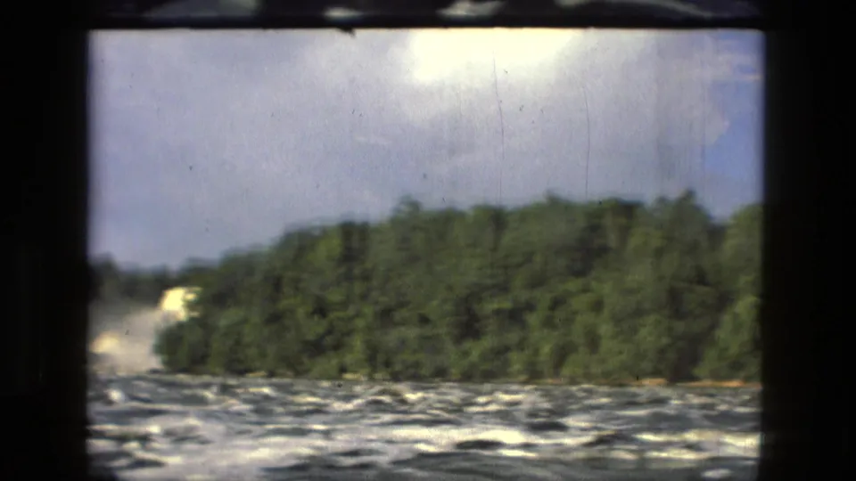 1979 Manaus, Brazil 8mm frame with rough river water, dense trees, bright sky, and a dark interior window edge.