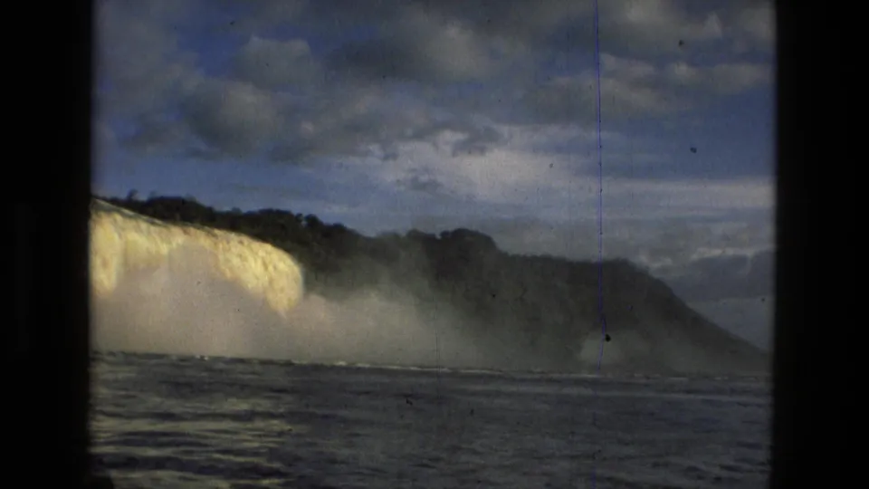 1979 8mm view near Manaus, Brazil, showing a wide waterfall, mist, river water, cloudy sky, and dark film-frame borders.