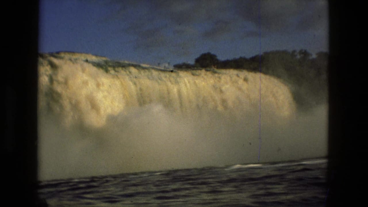 Wide waterfall pouring over a ledge with mist and dark water below.