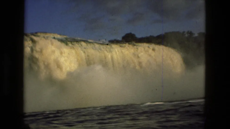 1979 8mm Manaus travel footage showing a broad waterfall, heavy spray, cloudy sky, and dark water in a handheld frame.