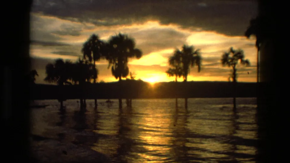 Final 1979 Manaus sunset view with silhouetted palms, shoreline, and shimmering water reflection.