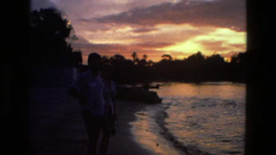1979 Manaus 8mm frame with two silhouetted figures near the water as sunset color reflects along the shore.