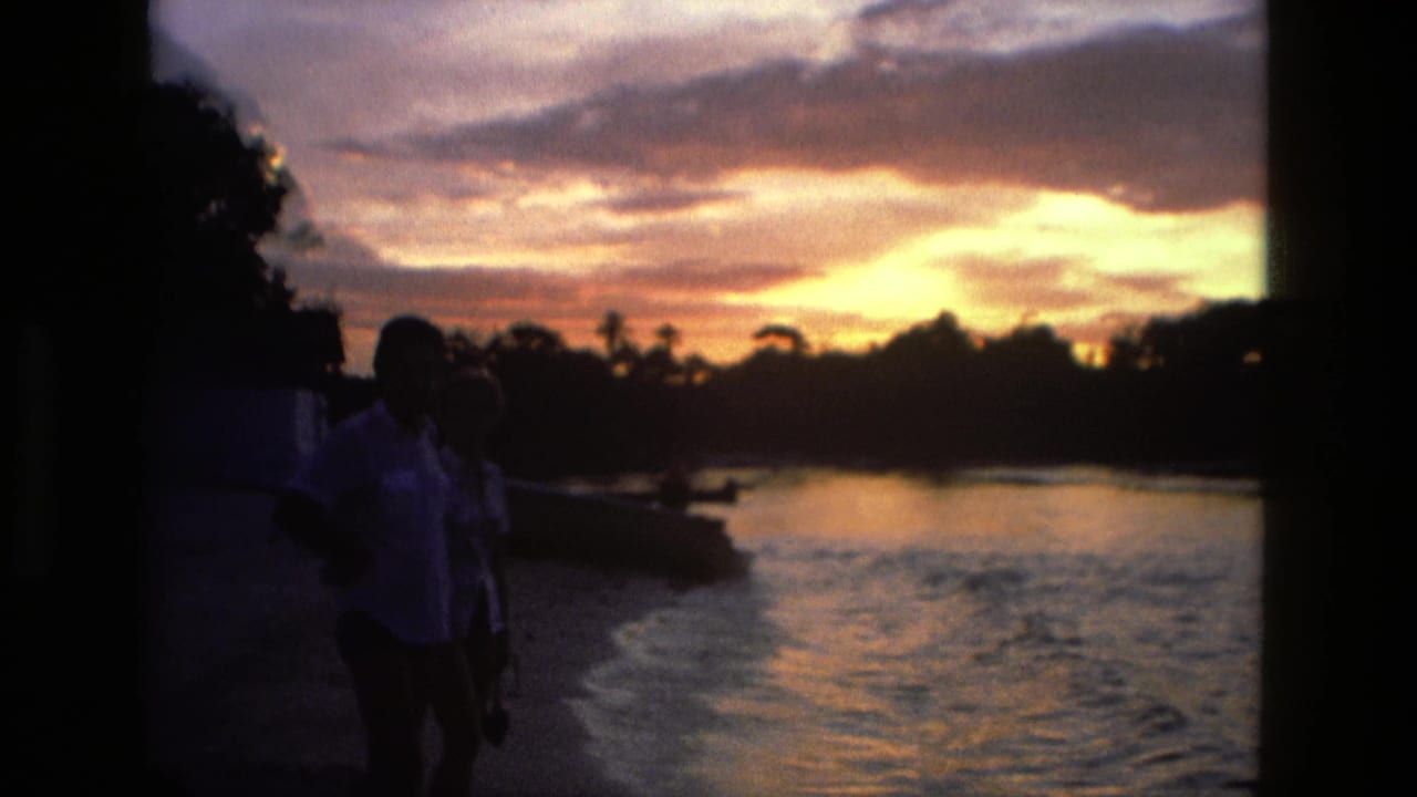 Silhouetted couple standing near a riverbank at sunset with glowing clouds and water reflections.