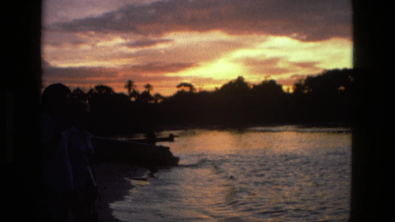 1979 8mm home-movie frame from Manaus, Brazil, showing shadowed figures near a lake as sunrise reflects on rippling water.