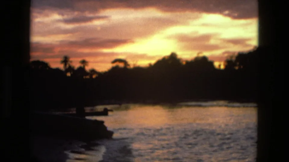 Manaus, Brazil 8mm frame with a glowing sunrise over water, dark tropical tree line, and a small shadowed shoreline form.