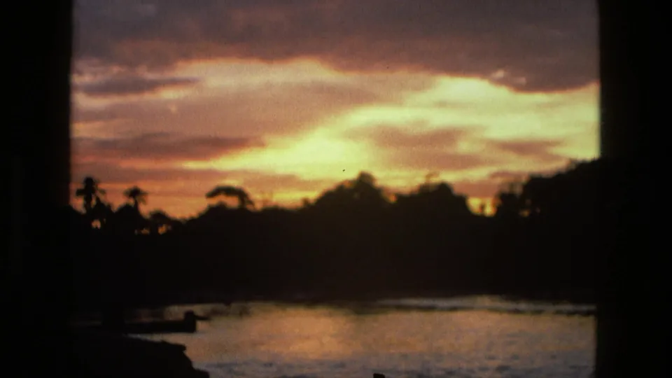 1979 Manaus 8mm frame emphasizing orange sunrise clouds, a dark tropical shoreline, and warm reflections on lake water.