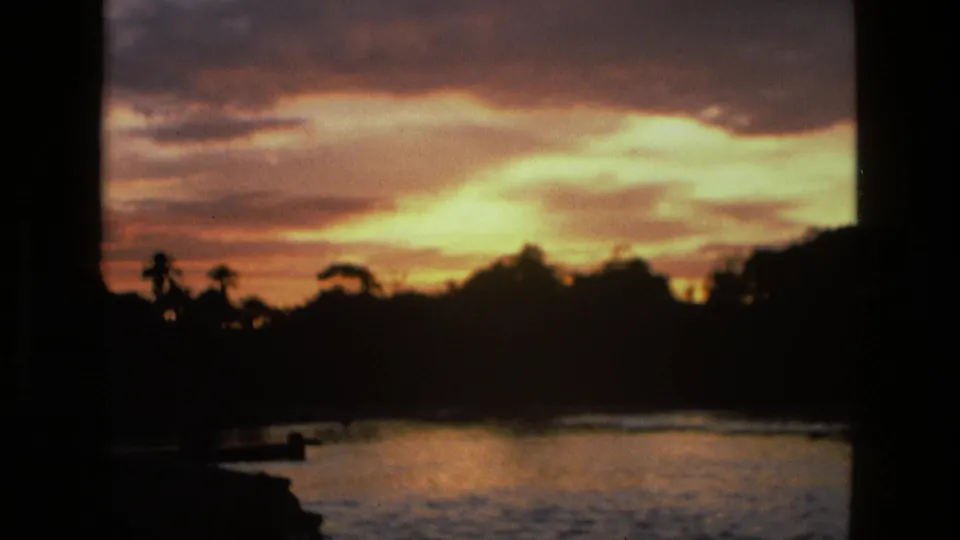 8mm home-movie frame from Manaus showing a glowing sunrise, dark palms and jungle edge, and reflected light on the lake.