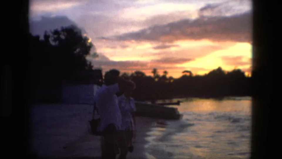 The couple remains near the Manaus river edge, seen in soft 8mm silhouette against orange and purple dusk light.
