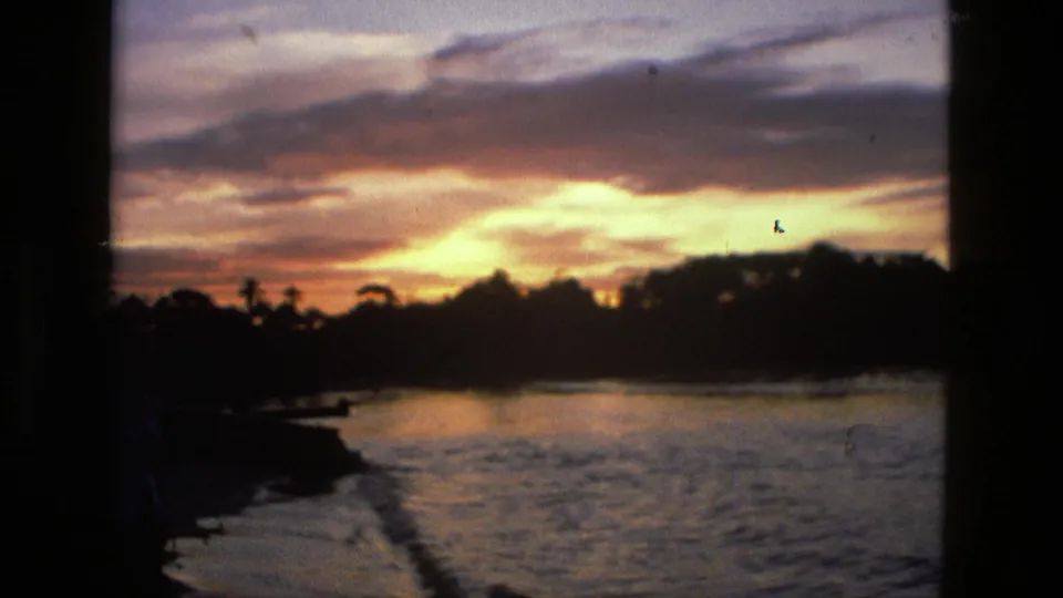A Manaus riverside sunset dominates the frame, with water, dark trees, and a partial person at the edge of the 8mm shot.