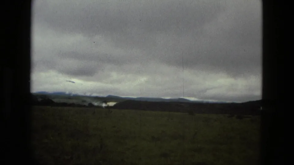 1979 8mm Manaus travel frame of an open grassy landscape under heavy clouds, with low hills in the distance.