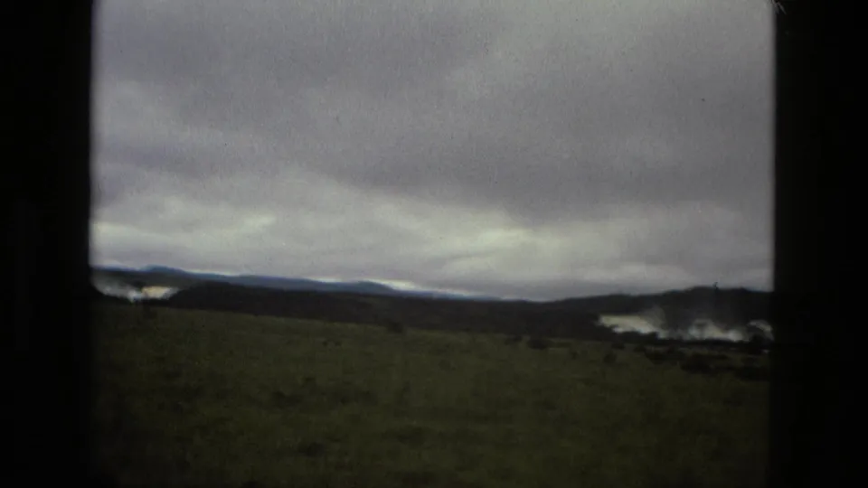1979 8mm Manaus footage showing a broad field, distant hills, and pale water or mist beneath a low gray sky.