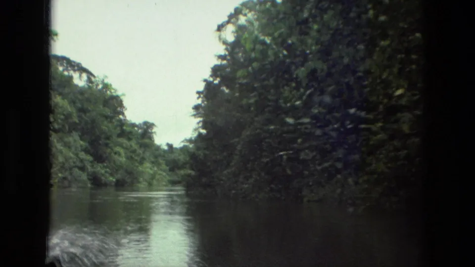 1979 8mm Amazon river view near Manaus, with forested banks, pale sky, and churning water from the moving boat.
