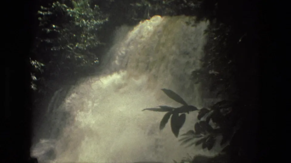 1979 8mm jungle waterfall view near Manaus, Brazil, with rushing water, spray, and silhouetted leaves in the foreground.