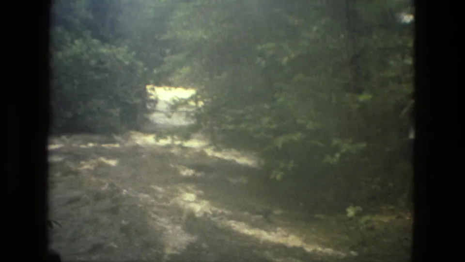 Vintage 8mm frame from Manaus, Brazil, showing a fast-flowing river corridor under soft, hazy light.