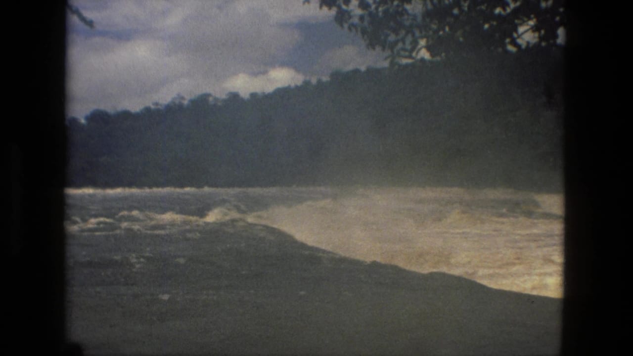 1979 8mm home-movie view near Manaus, Brazil, showing pale rushing rapids, dark foreground rock, wooded hills, and overhanging branches.
