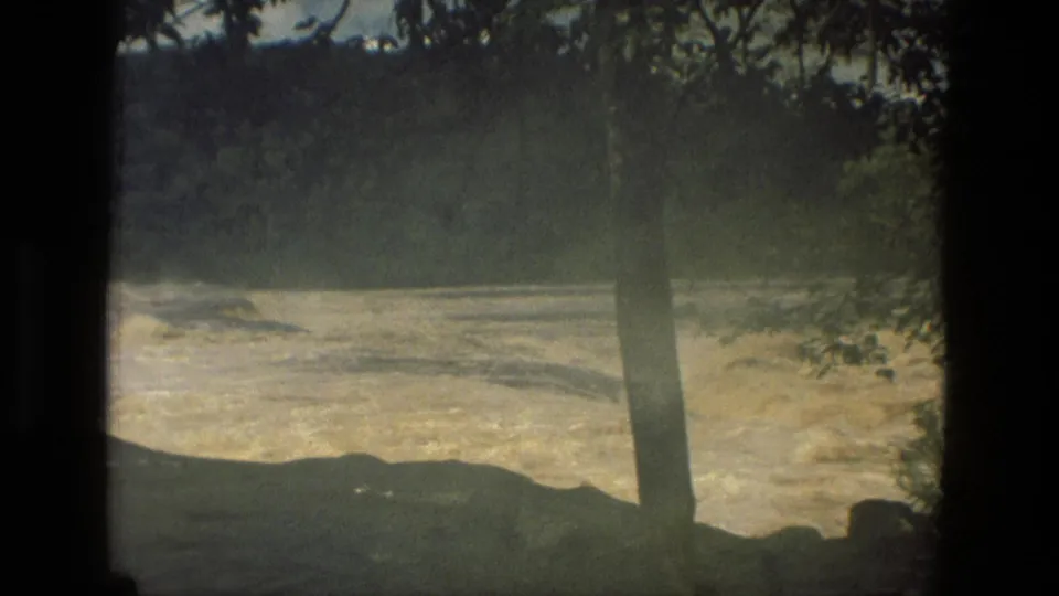 1979 Manaus, Brazil 8mm home-movie frame showing churning rapids, a foreground tree trunk, dark rocks, and dense green hills.