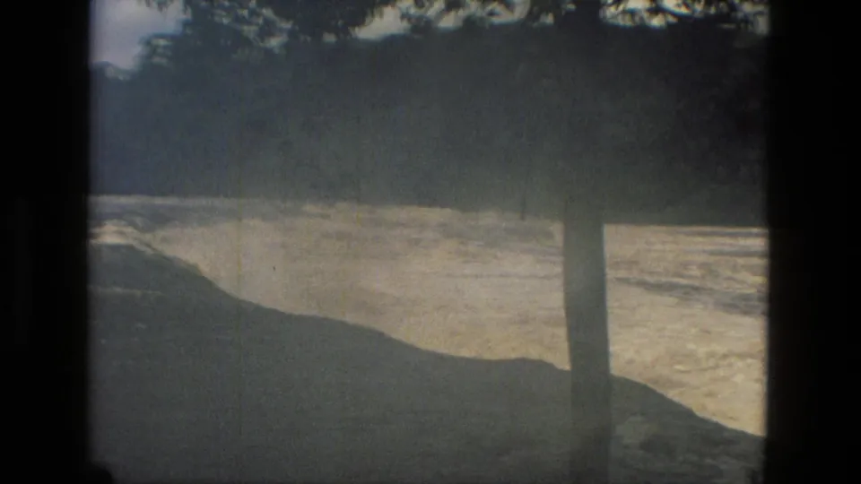 1979 Manaus frame showing a small figure near a very full river, partly hidden by trees and shadow.