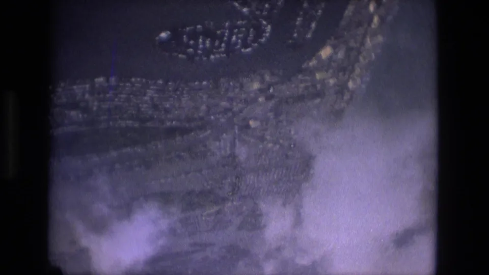 High-altitude 8mm view over Manaus with water, shoreline, and urban areas softened by haze and film grain.