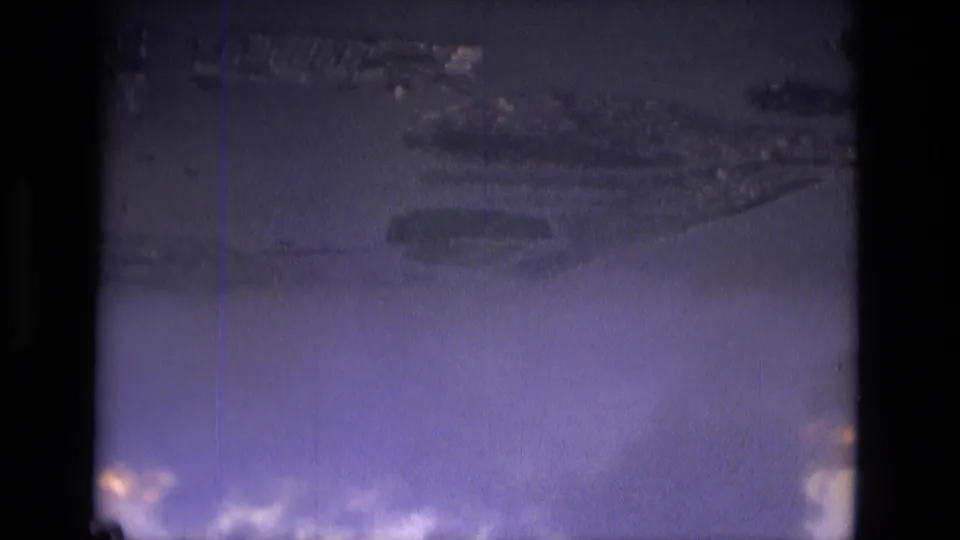 1979 8mm aerial view near Manaus with clouds, faint ground forms, a vertical scratch, and purple-blue film color.