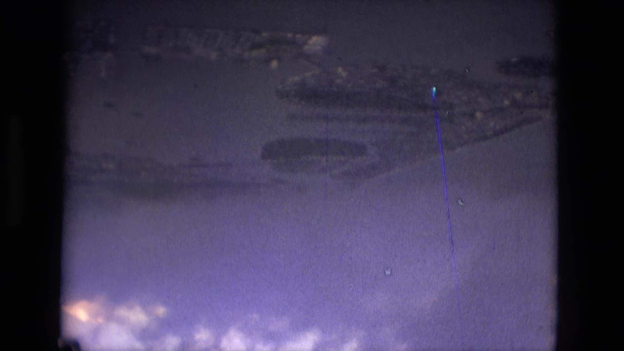 Blue-purple aerial view of water and distant land shapes with dark film borders.