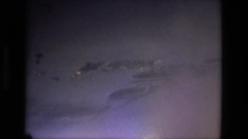 Blue-tinted 8mm aerial frame from the 1979 Brazil travel footage, showing a long island or shoreline form across open water.