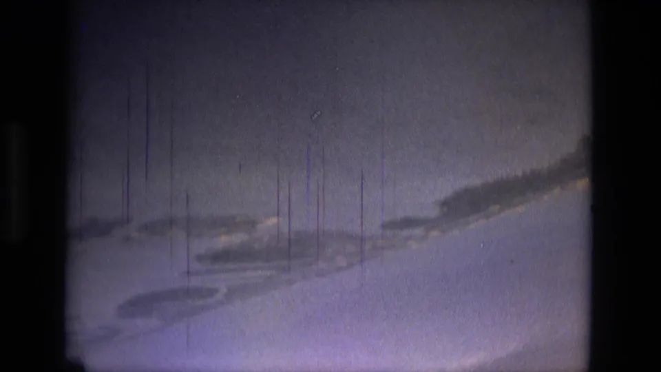 Blue-purple 8mm frame from 1979 Brazil travel footage showing water, a curved landform, and prominent vertical film scratches.