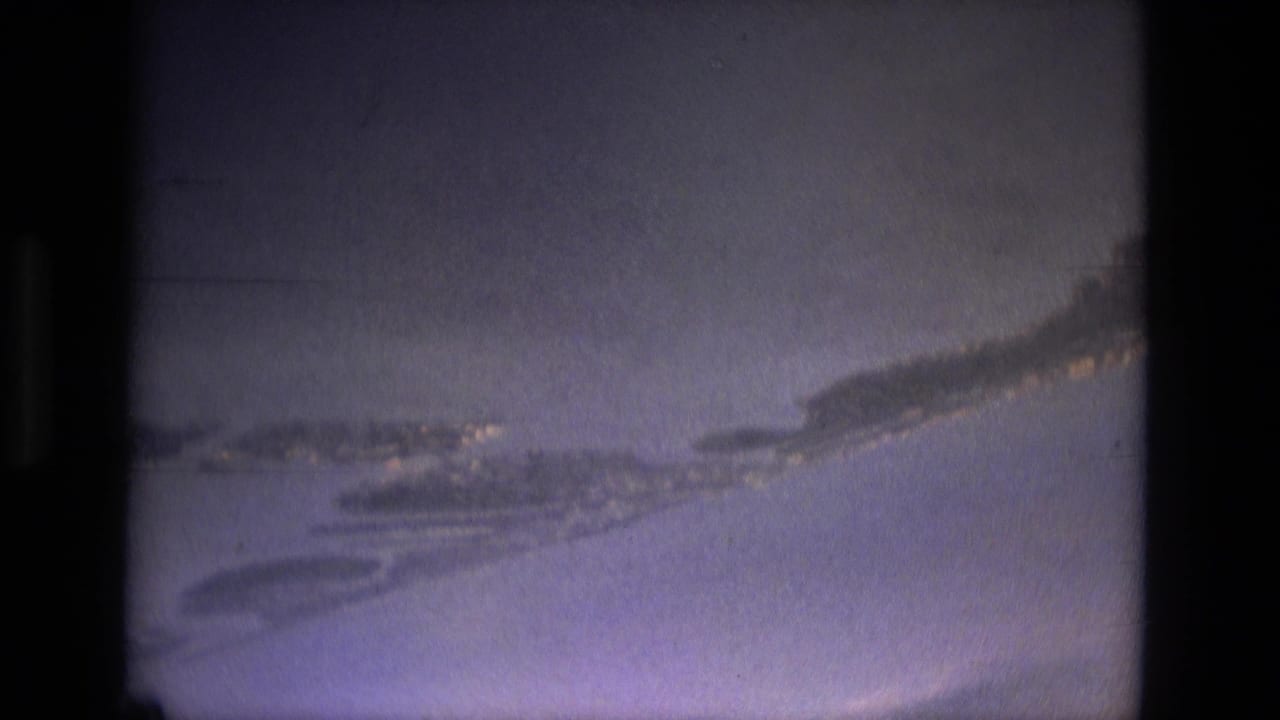 Soft blue-gray aerial view with white cloud streaks and dark film borders.