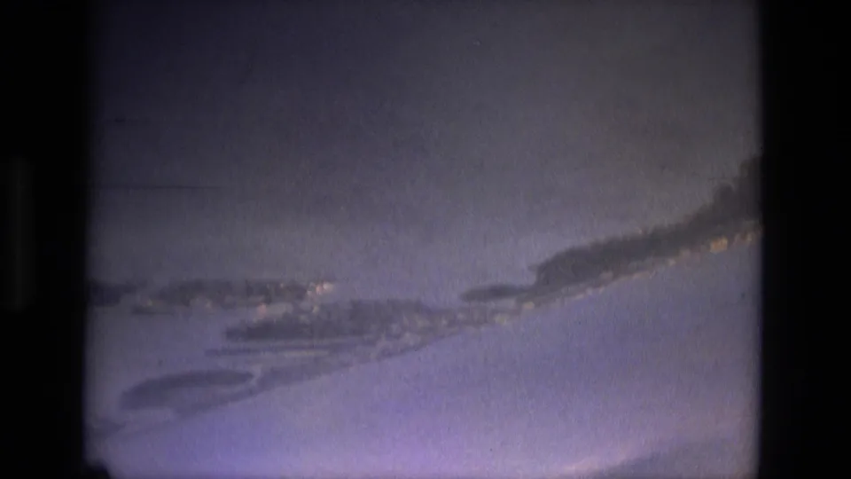 1979 8mm frame showing a hazy blue aerial view with pale cloud streaks and heavy dark borders from the film scan.