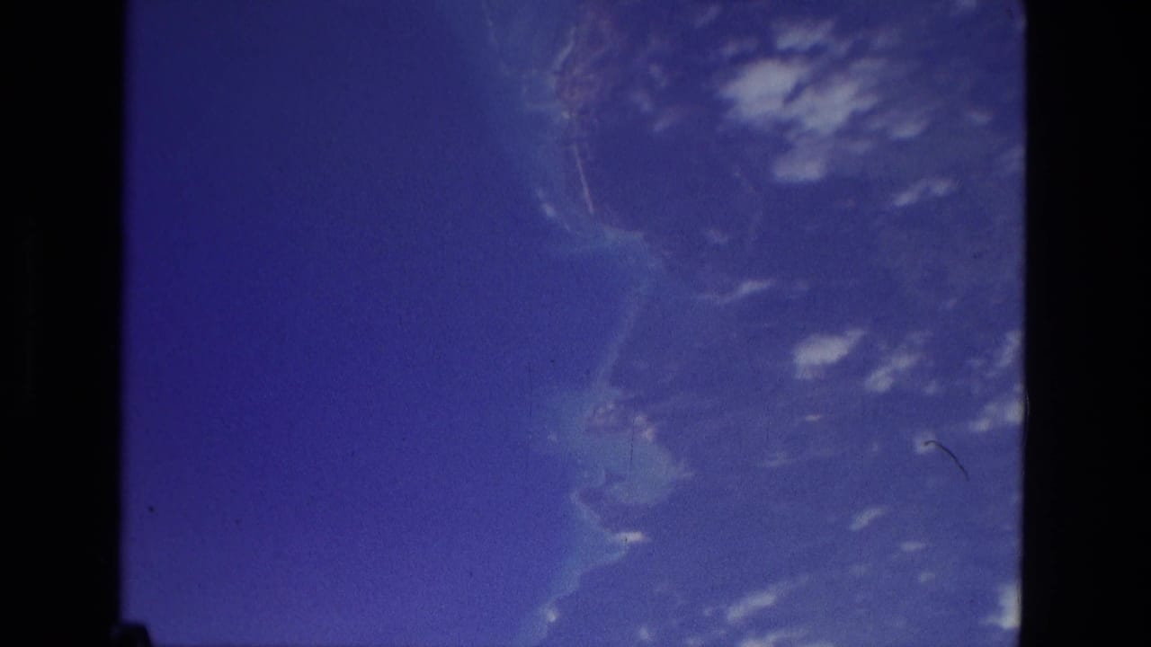 1979 Manaus 8mm frame showing blue sky, scattered cloud shapes, and soft distant land or water tones within dark film edges.