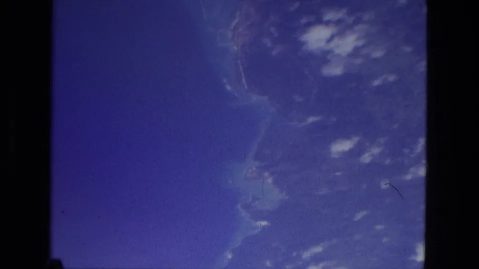 1979 Manaus 8mm frame showing blue sky, scattered cloud shapes, and soft distant land or water tones within dark film edges.