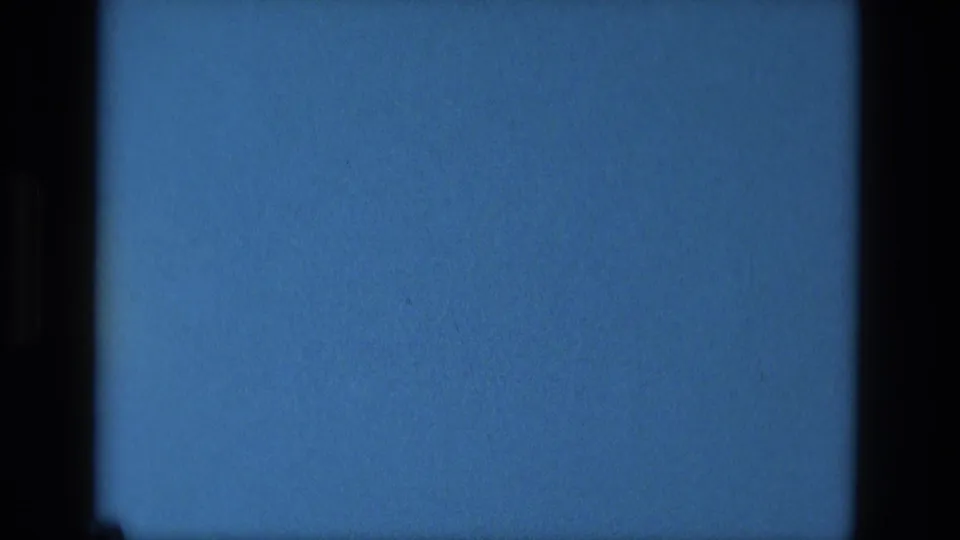 1979 8mm home-movie frame from Manaus metadata showing a static blue field, dark film borders, grain, and minor specks.