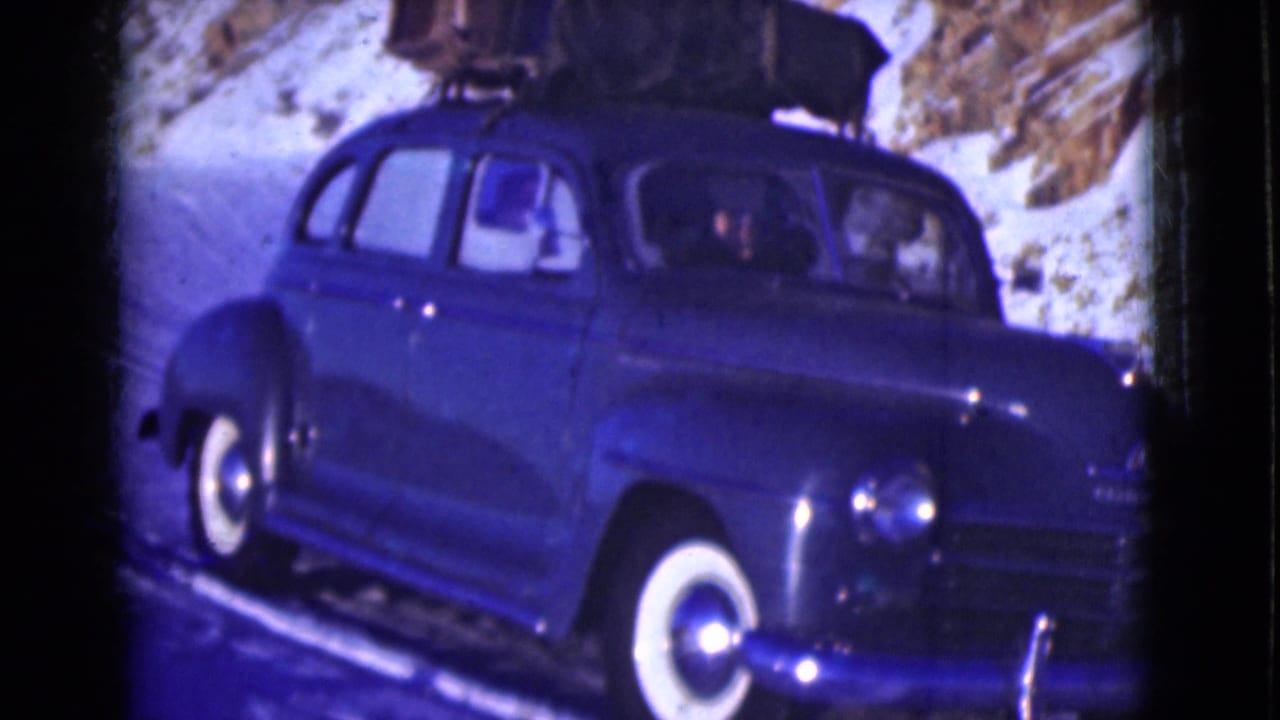 Blue sedan seen closer on a snowy roadside with luggage strapped above.