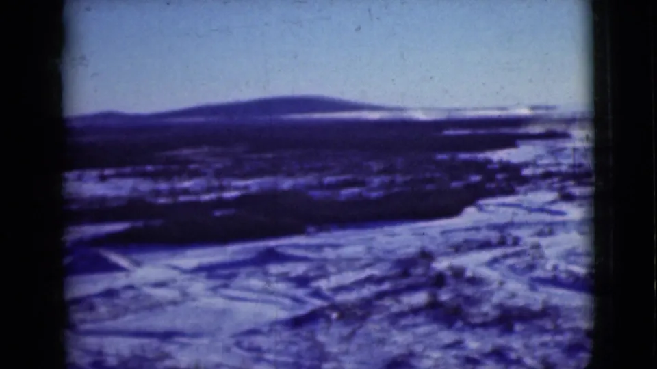 Snow-covered Alaska landscape with low hills and dark brush, seen after the car sequence.
