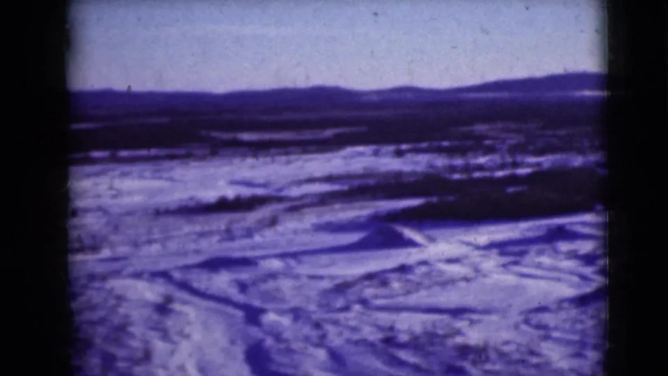 Blue-purple 8mm frame showing an Alaskan snowfield, uneven frozen ground, rolling hills, and far mountain silhouettes.