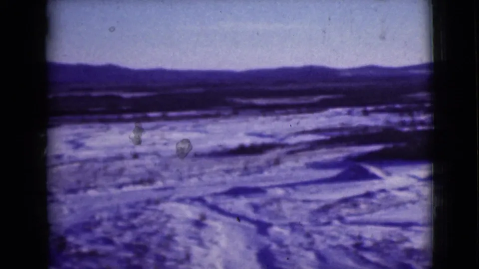 Final 1946 8mm view of Alaska winter terrain, with a broad snowy field, dark ridge line, and distant mountains under a pale sky.
