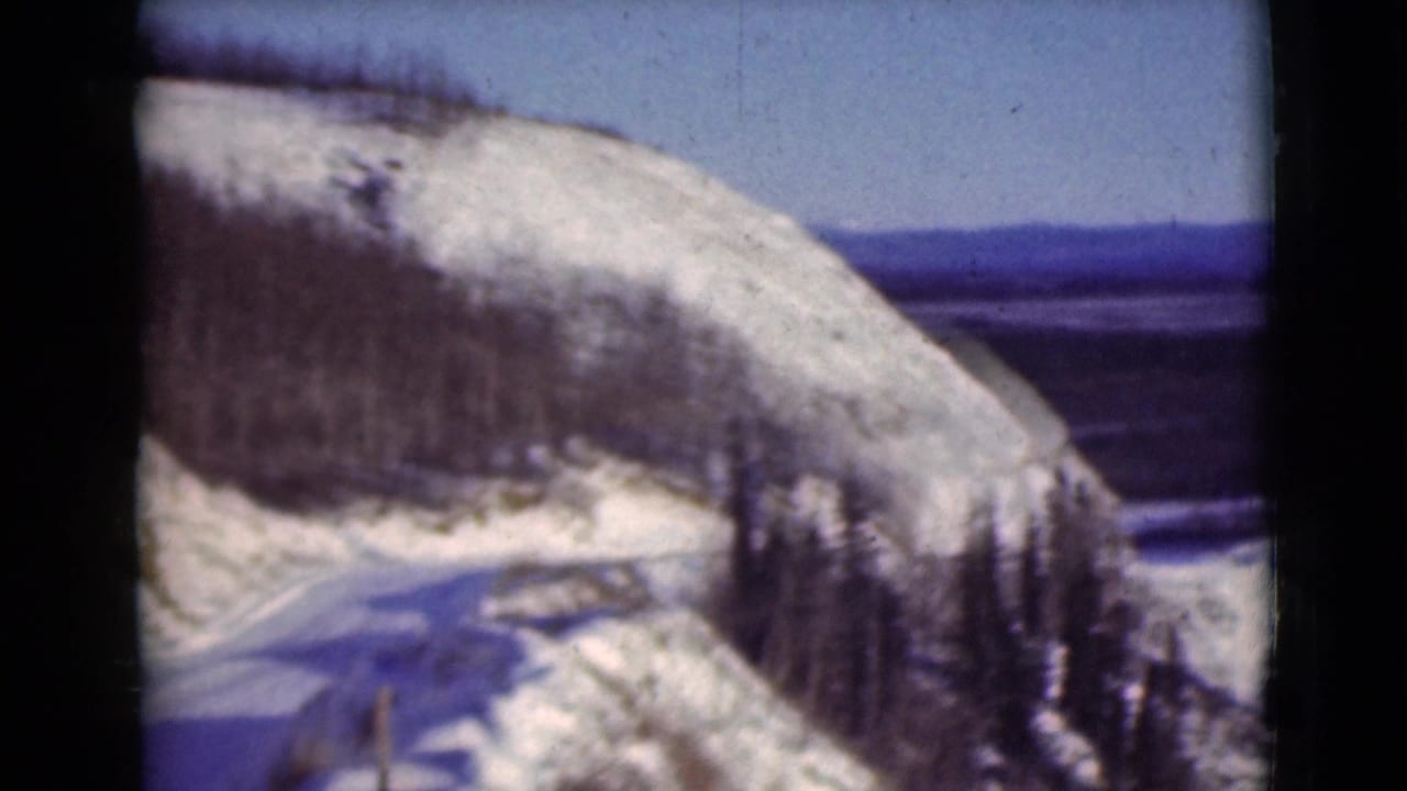Snowy mountainside road with evergreen trees and distant landscape visible through film borders.