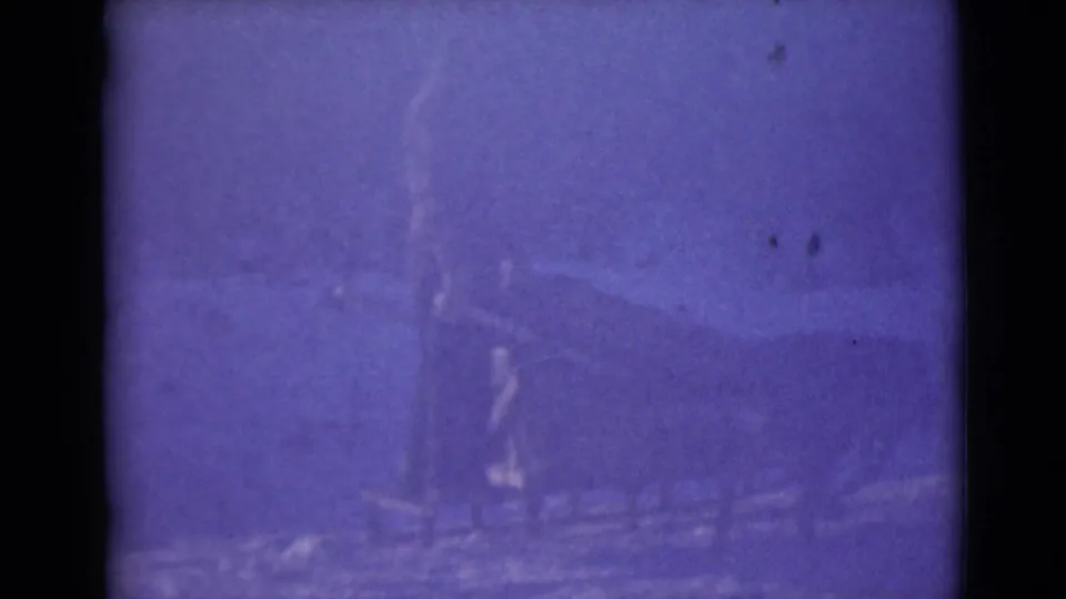 1946 Alaska 8mm frame showing a blurred dog team and sled-like shape moving across snowy terrain.