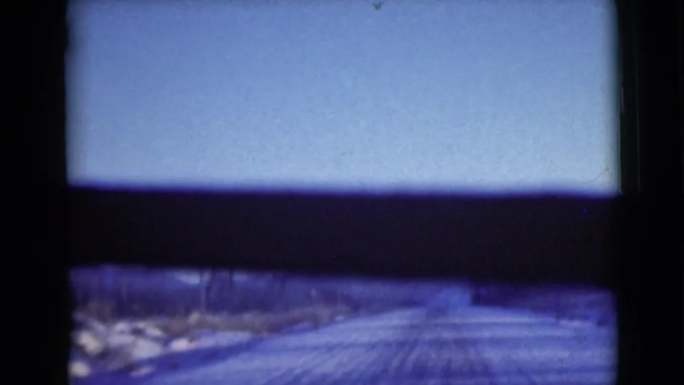 1946 Alaska travel frame showing a snow-covered road receding through open winter terrain with dark framing from the camera or vehicle.