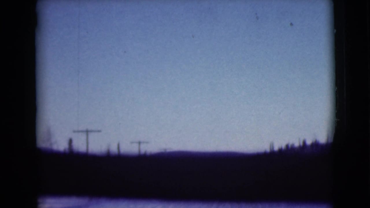 Hazy sky over a dark horizon with utility poles and film gate borders.