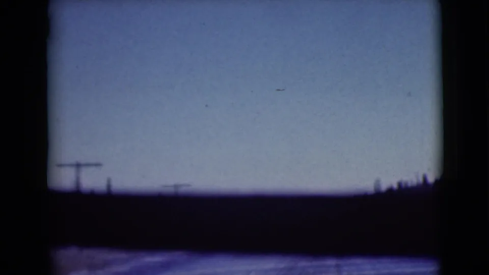 1946 Alaska 8mm view of utility poles, low hills, and sparse trees seen from a moving road perspective.