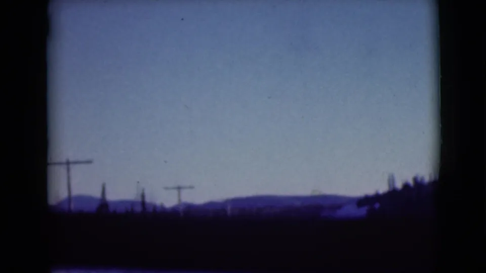 1946 Alaska 8mm view of distant hills, utility poles, pale sky, and dark roadside silhouettes from a moving vehicle.