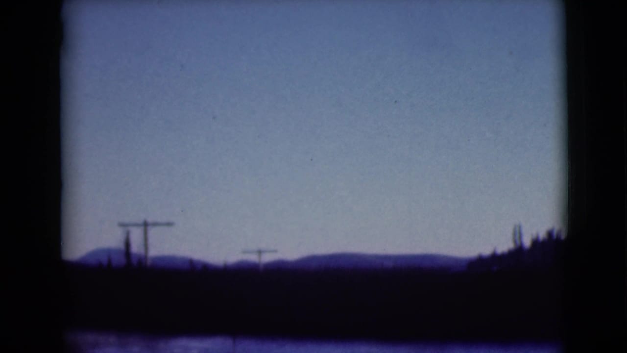 1946 Alaska travel frame showing a low mountain horizon, roadside utility poles, and dark foreground seen through a vehicle window.