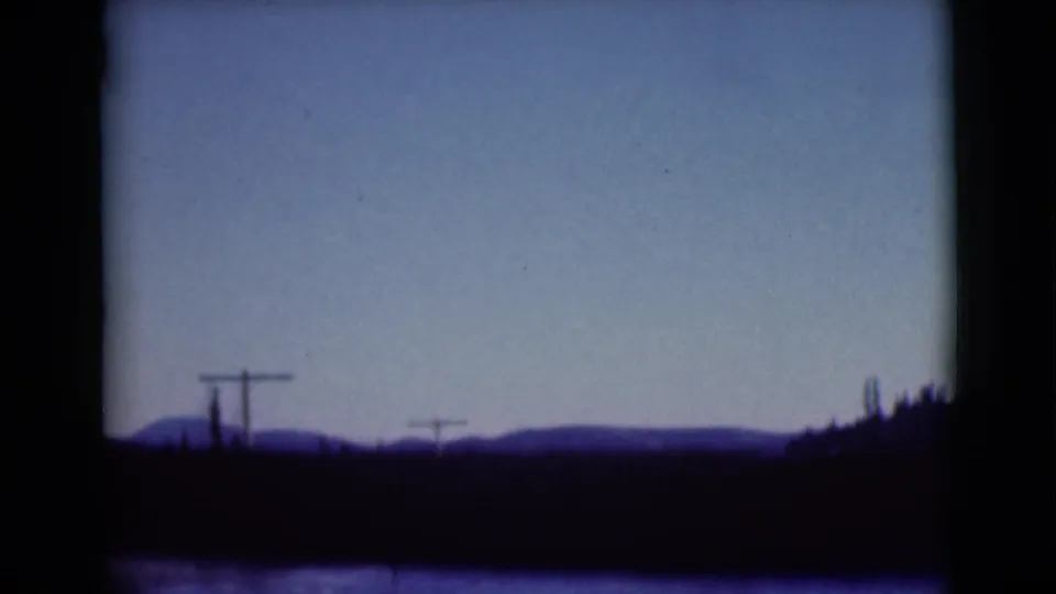 1946 Alaska travel frame showing a low mountain horizon, roadside utility poles, and dark foreground seen through a vehicle window.