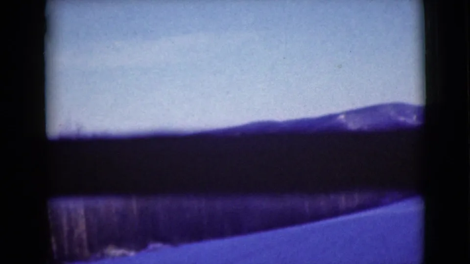 1946 Alaska road-travel view with a snowy foreground, dark tree line, and broad mountain ridge under a pale sky.