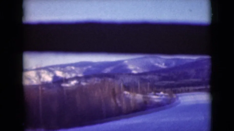 1946 Alaska 8mm frame showing a snow-covered road bordered by trees, with distant mountains and a blue-purple film cast.