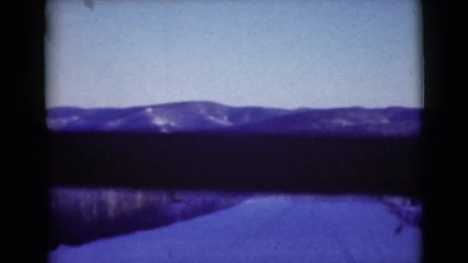 1946 Alaska home-movie frame from a moving vehicle, looking along a snowy road toward forested slopes and mountains.