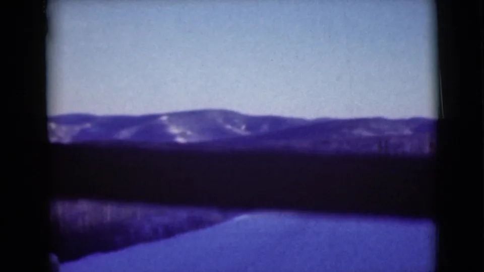Soft 8mm frame from 1946 Alaska showing a dark foreground, snowy road edge, pale sky, and distant mountain ridge.