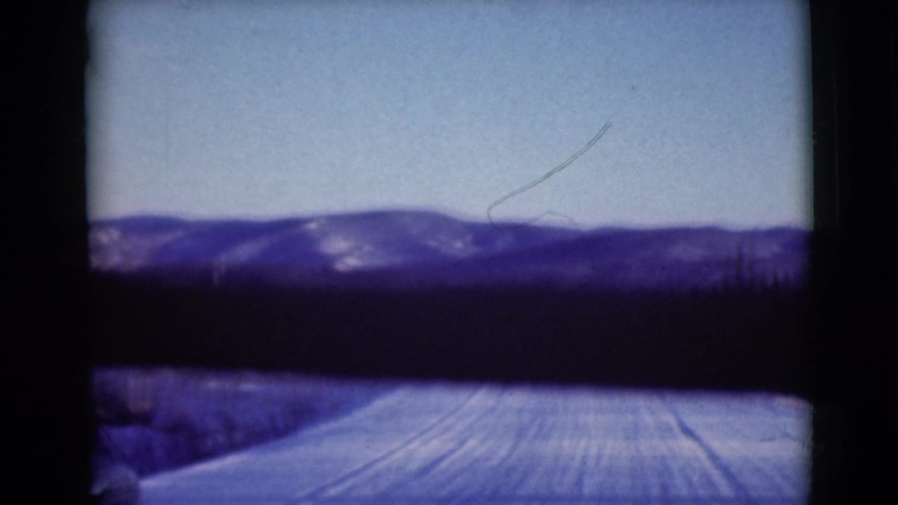 Snowy road and distant mountain ridge under blue sky, seen through dark 8mm frame borders.