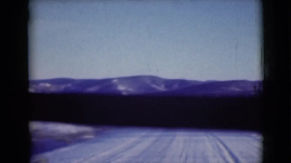 1946 Alaska home-movie still with vehicle-level view of a snowy road approaching low mountain ridges.