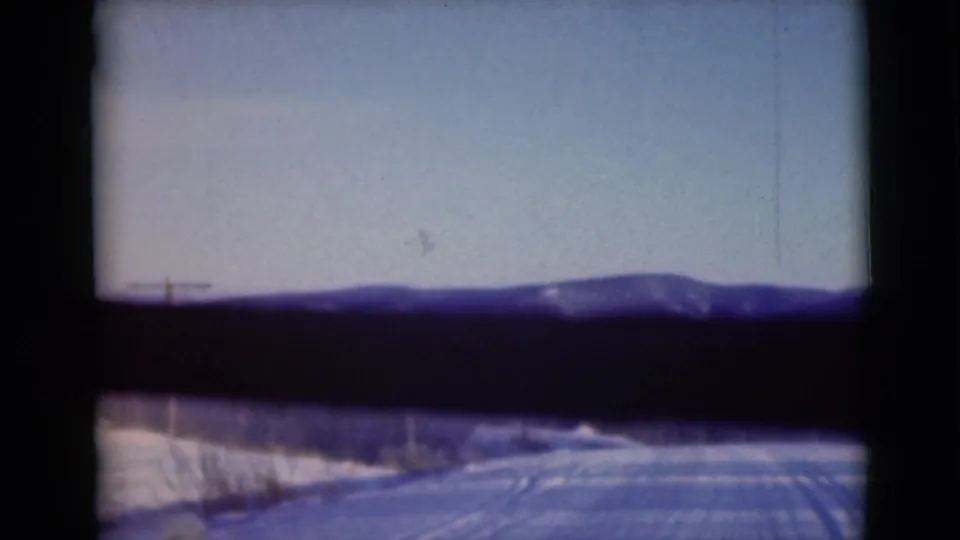 1946 Alaska 8mm frame with a low snow-dusted mountain ridge and pale blue sky above a dark foreground band.